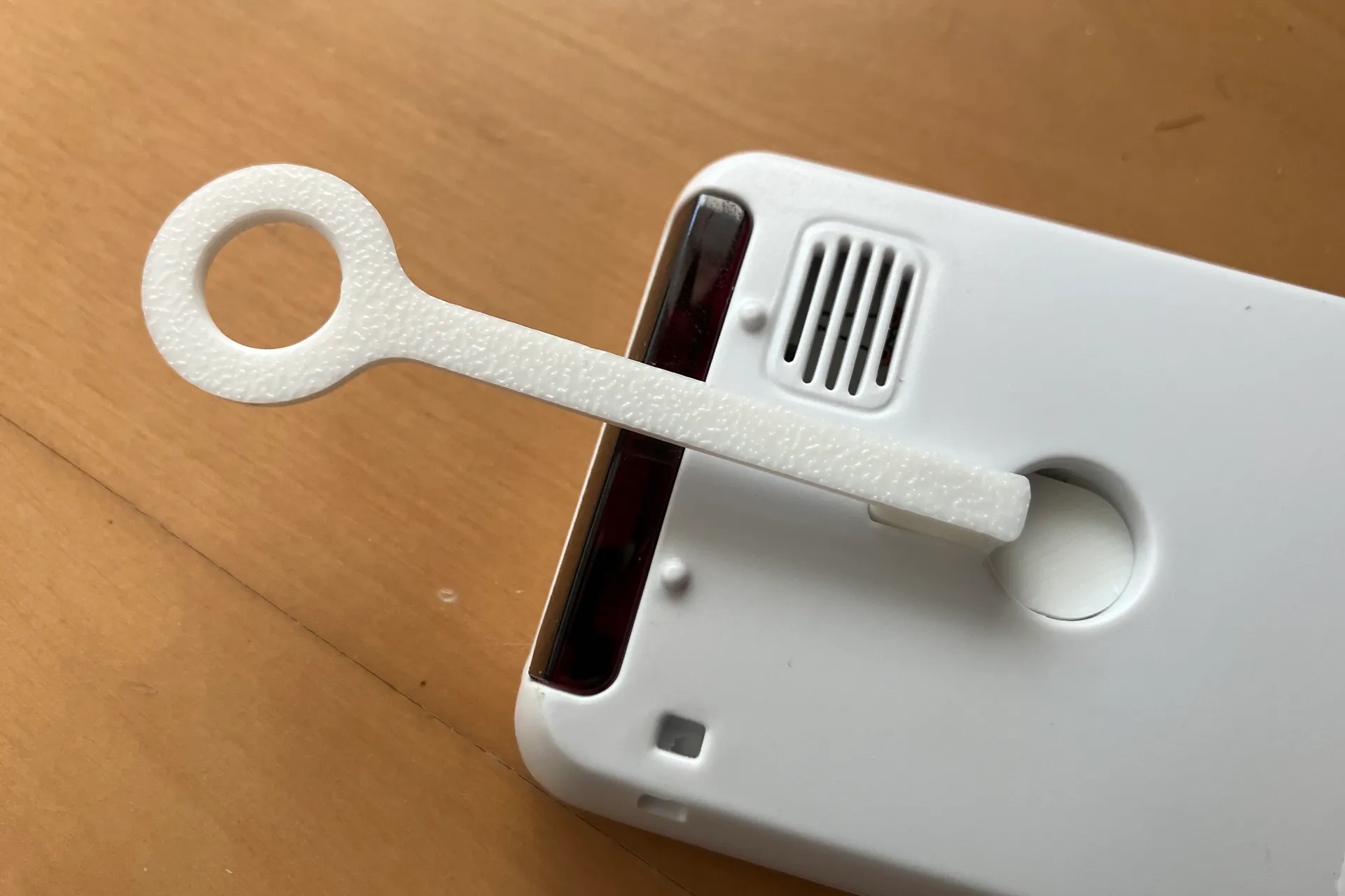 エアコンのリモコンの裏面の穴に作成した部品が取り付けられ、上側に丸い輪が出ている。